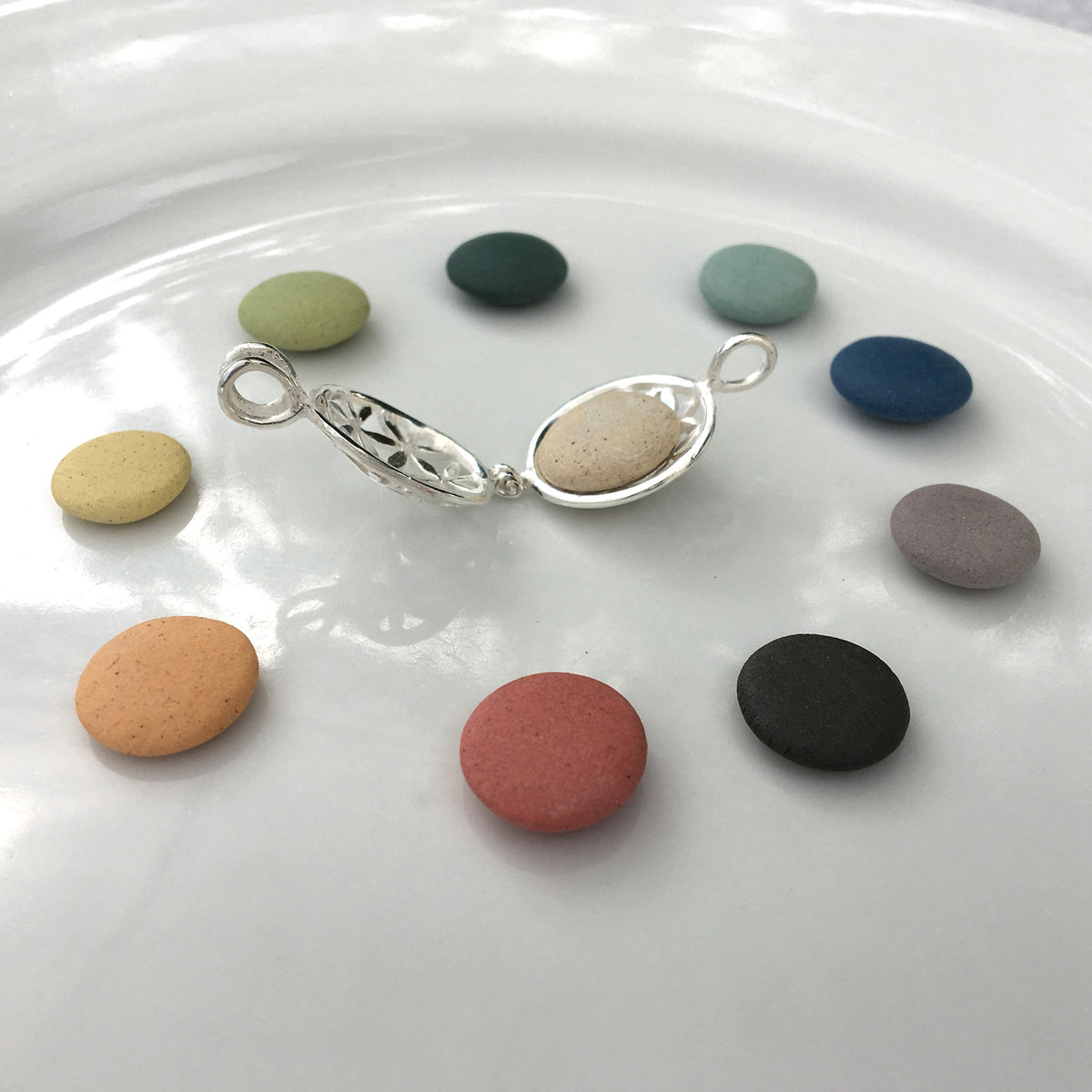 colour options of pebbles in a white dish with an open silver locket in the middle