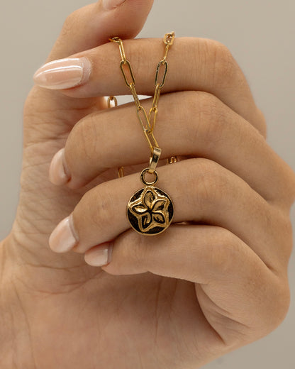 Close-up of a hand holding a gold chain with a round pendant featuring a floral design, showcasing the elegant Charm Bracelet.