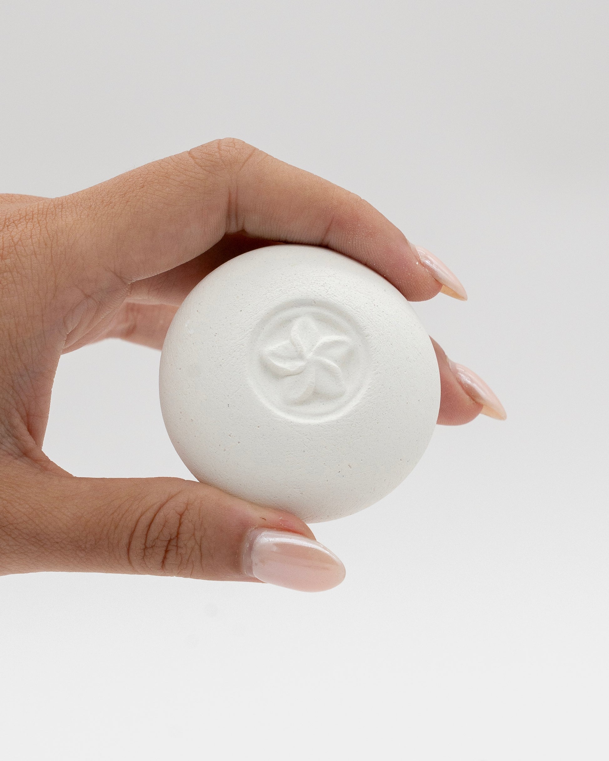 Hand holding a white round Scent Pebble with a subtle embossed flower design, showcasing its smooth texture against a neutral background.