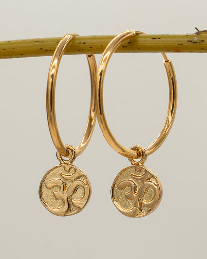 Gold hoop earrings with 'Om' symbol charms on a light gray background