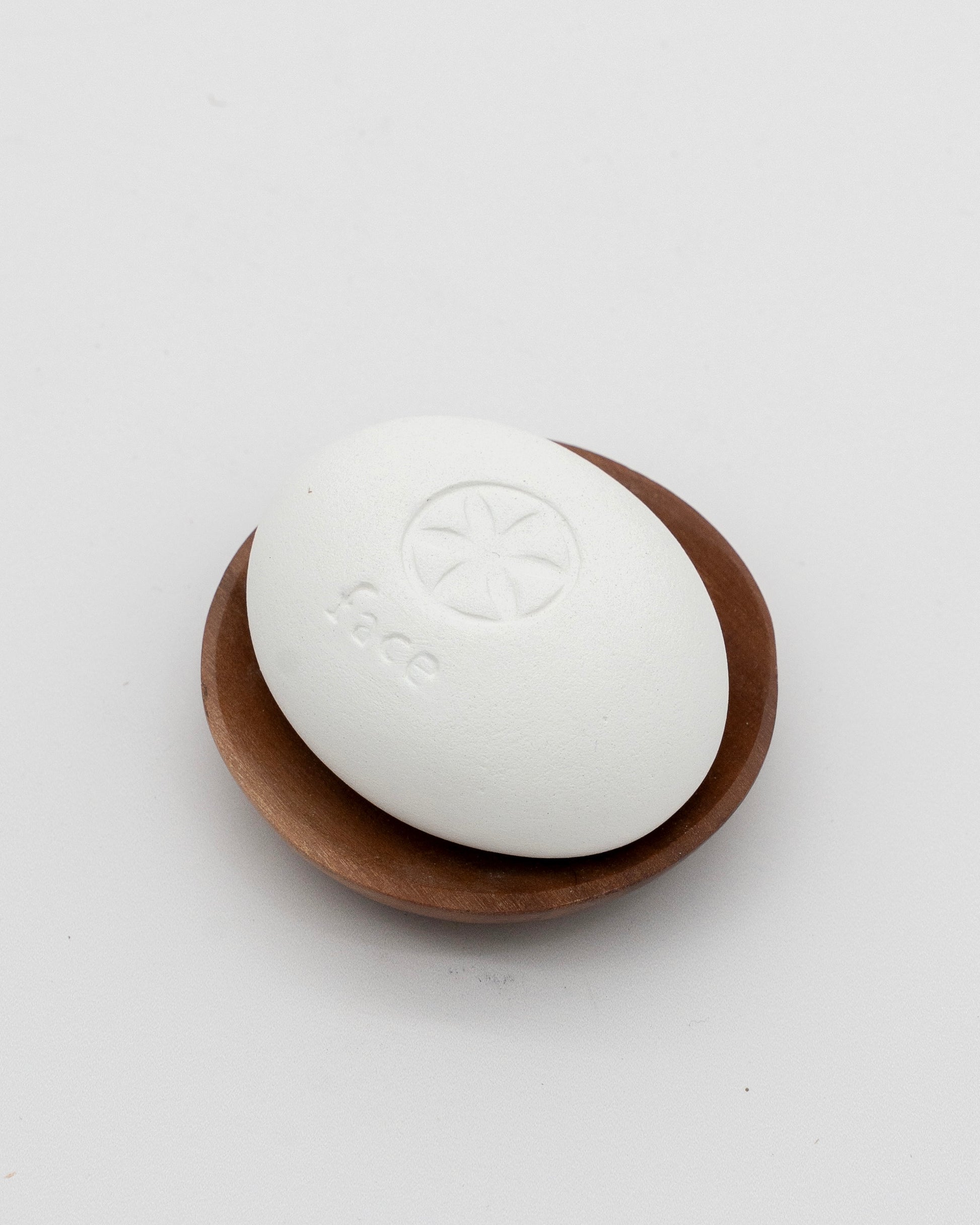 White Face Pebble resting on a small wooden dish, designed for gentle exfoliation and myofascial massage in skincare routines.