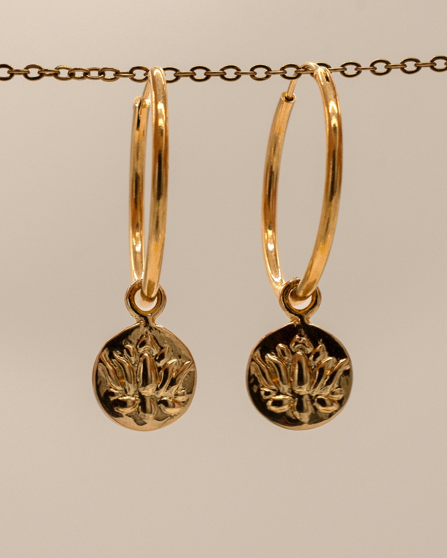 Gold hoop earrings with circular pendants on a beige background
