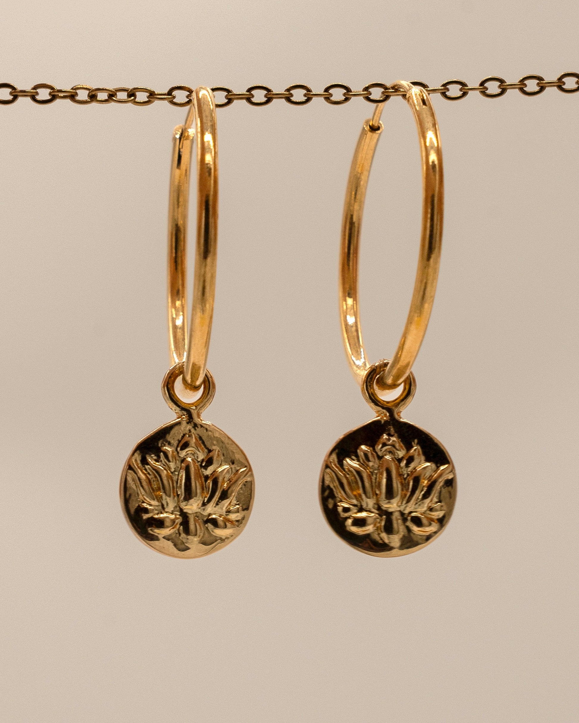 Gold hoop earrings with circular pendants on a beige background