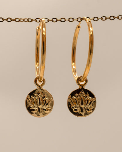 Gold hoop earrings with circular pendants on a beige background