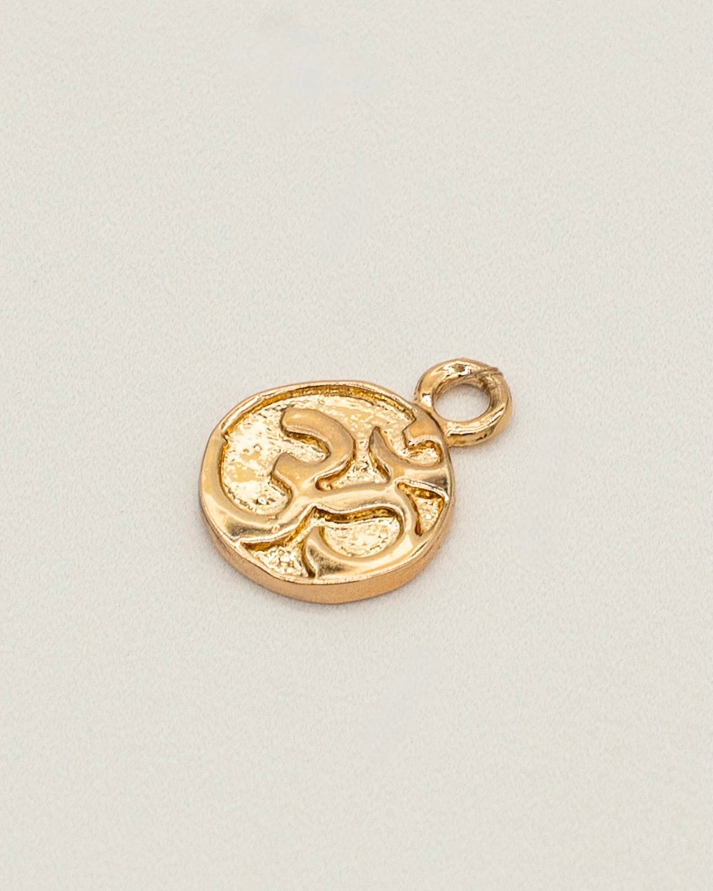 Close-up of a small, round gold charm with a textured surface and abstract design, suitable for use with Charm Earrings.