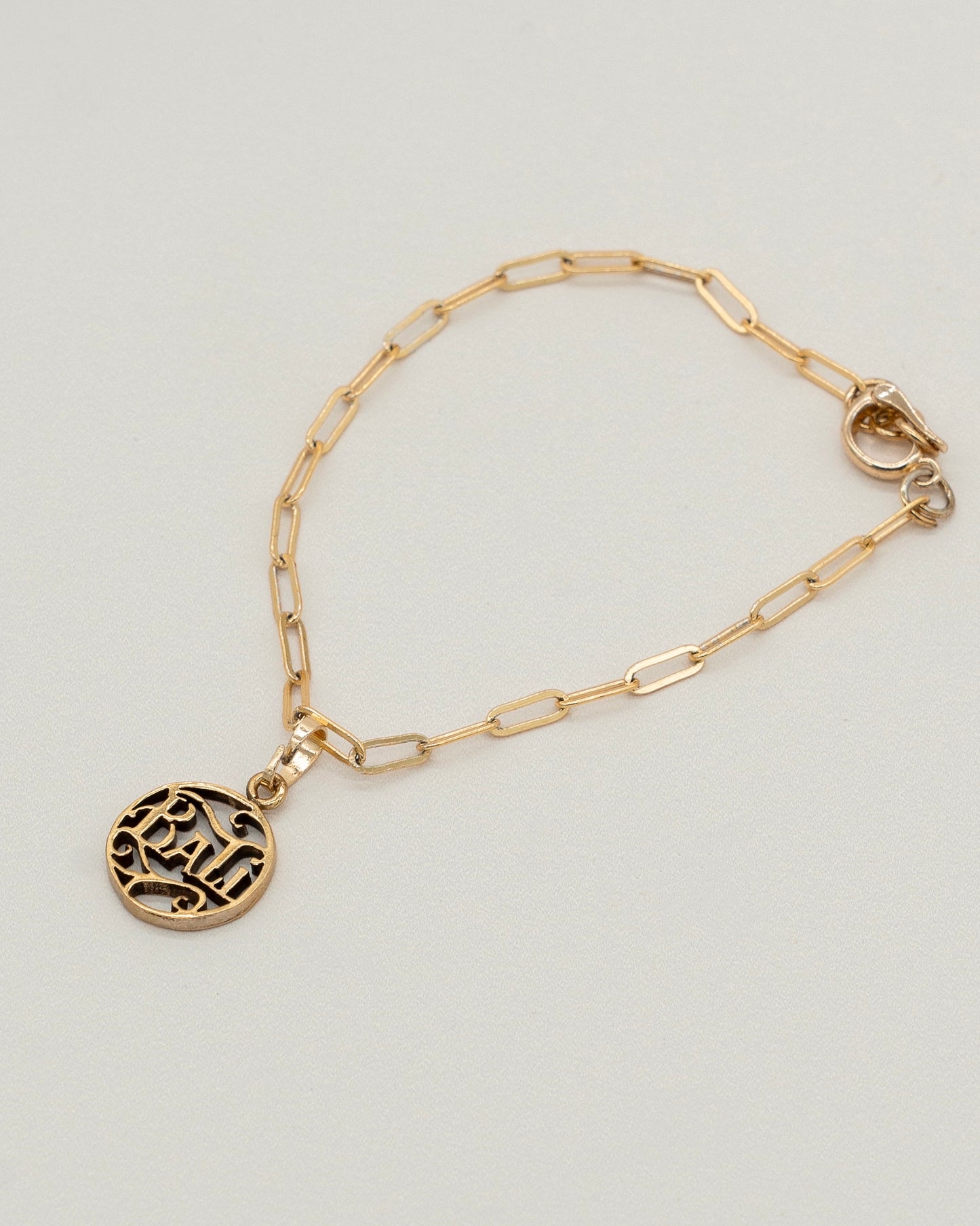 Delicate gold Charm Bracelet with a paperclip chain and a round engraved pendant, designed for elegant everyday wear and versatile styling.