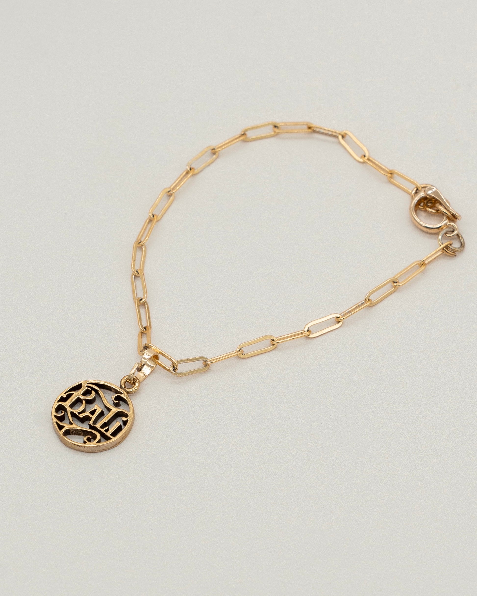 Delicate gold Charm Bracelet with a paperclip chain and a round engraved pendant, designed for elegant everyday wear and versatile styling.