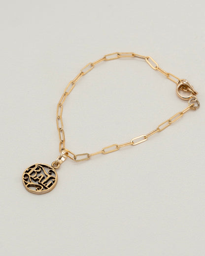 Delicate gold Charm Bracelet with a paperclip chain and a round engraved pendant, designed for elegant everyday wear and versatile styling.
