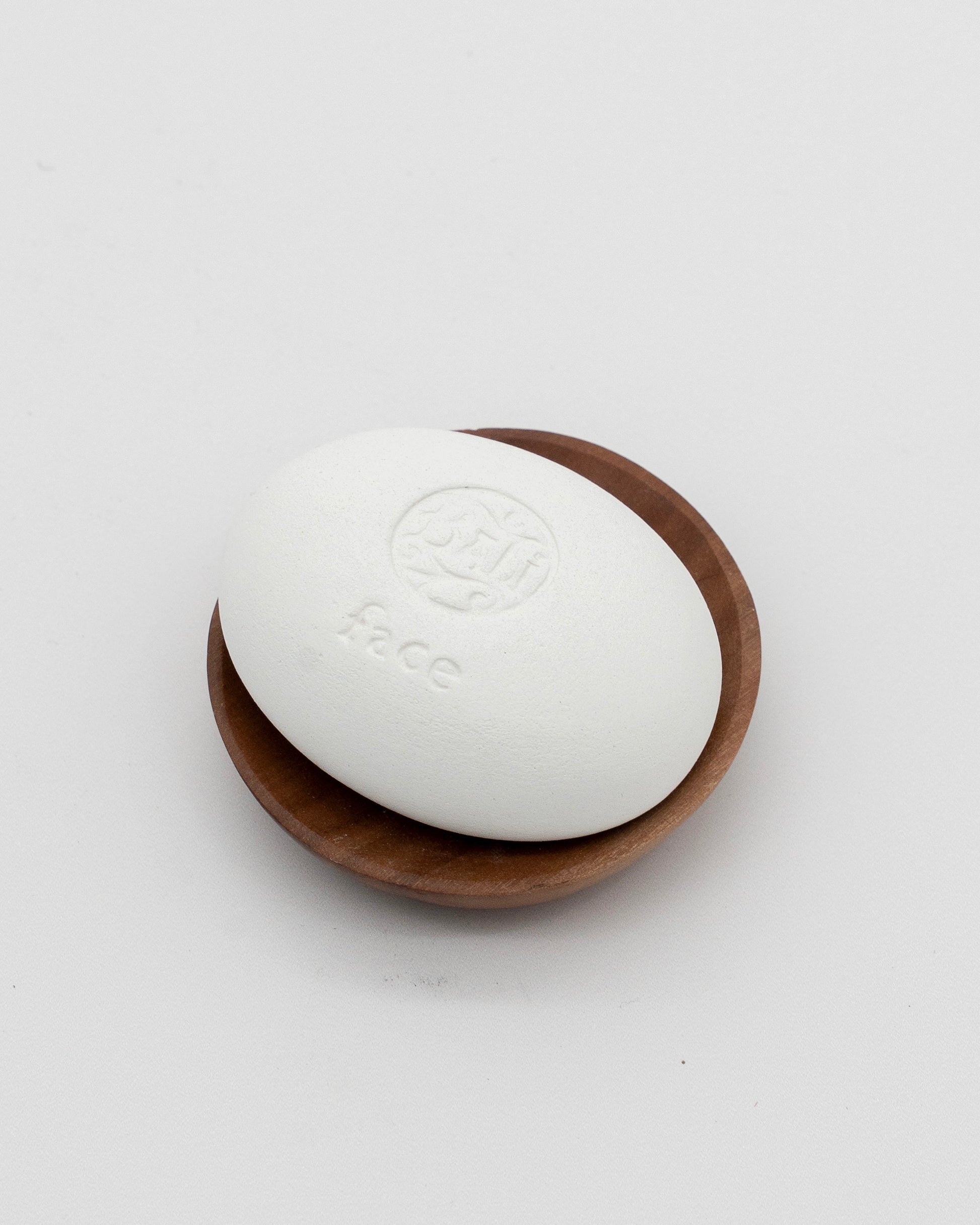 Face Pebble, a smooth white exfoliating tool resting on a small wooden dish, designed for gentle myofascial massage and skincare rituals.