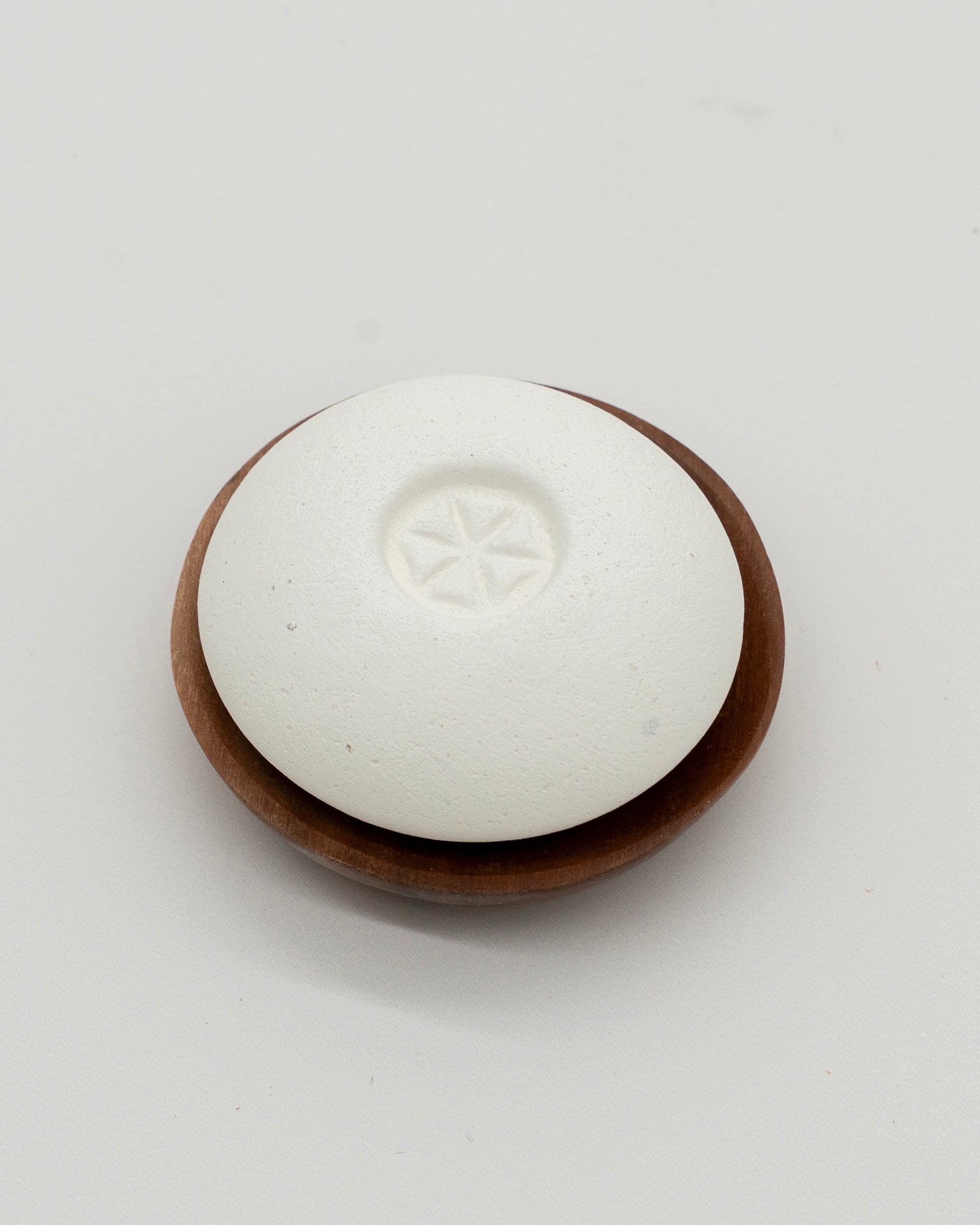 White smooth Scent Pebble with subtle star design in center resting on a round wooden dish, designed for aromatherapy and eco-friendly use.