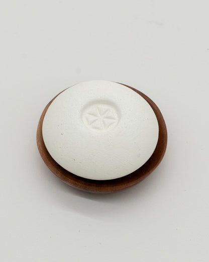 White smooth Scent Pebble with subtle star design in center resting on a round wooden dish, designed for aromatherapy and eco-friendly use.