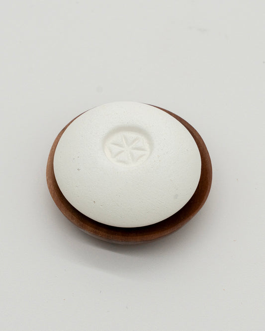 White smooth Scent Pebble with subtle star design in center resting on a round wooden dish, designed for aromatherapy and eco-friendly use.