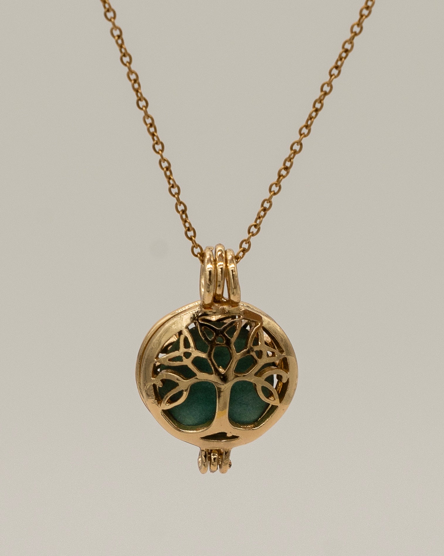 Gold Scent Locket featuring an intricate tree of life design in gold with a green aromatherapy insert, hanging from a delicate gold chain necklace.
