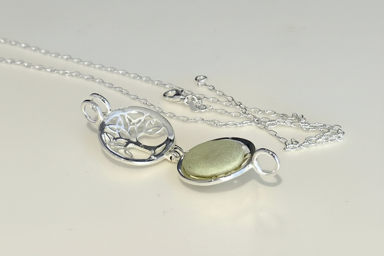 Silver necklace with a tree of life pendant and green stone on a light background