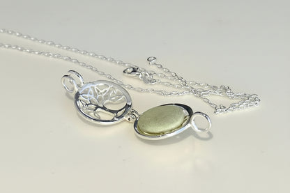 Silver necklace with a tree of life pendant and green stone on a light background