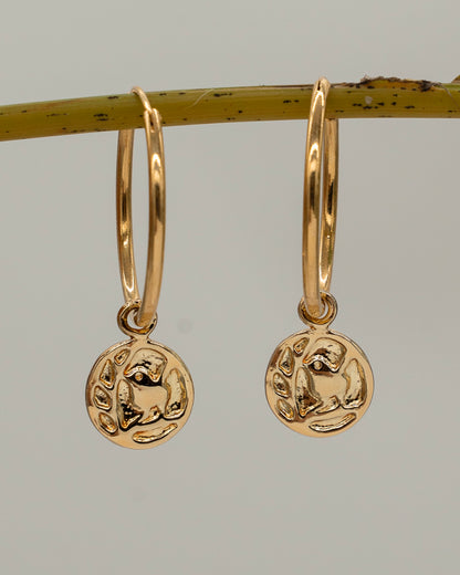 Gold hoop earrings with circular pendants on a branch