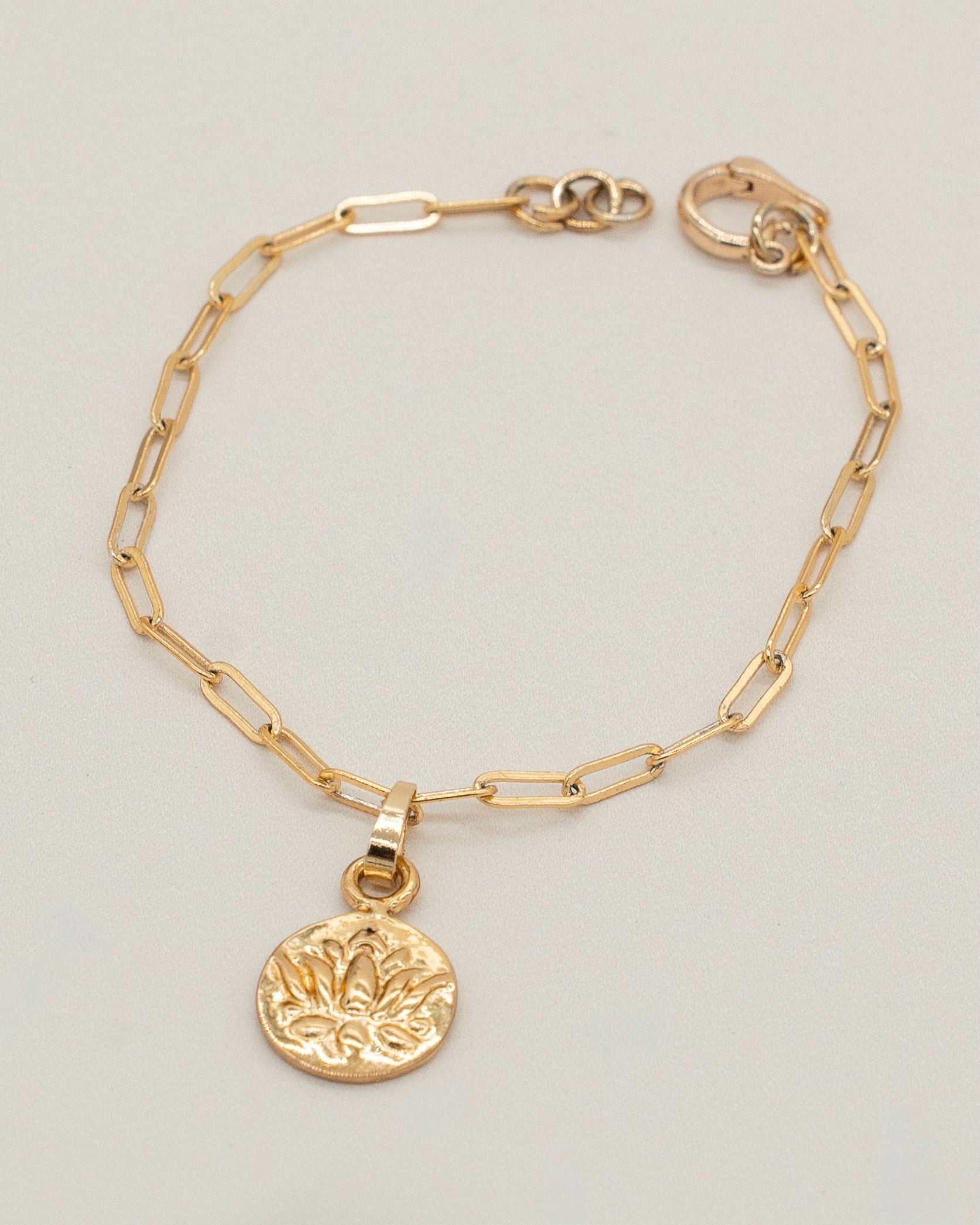 Delicate gold chain Charm Bracelet featuring an oval-link design and a round embossed charm with a floral motif, perfect for elegant everyday wear.