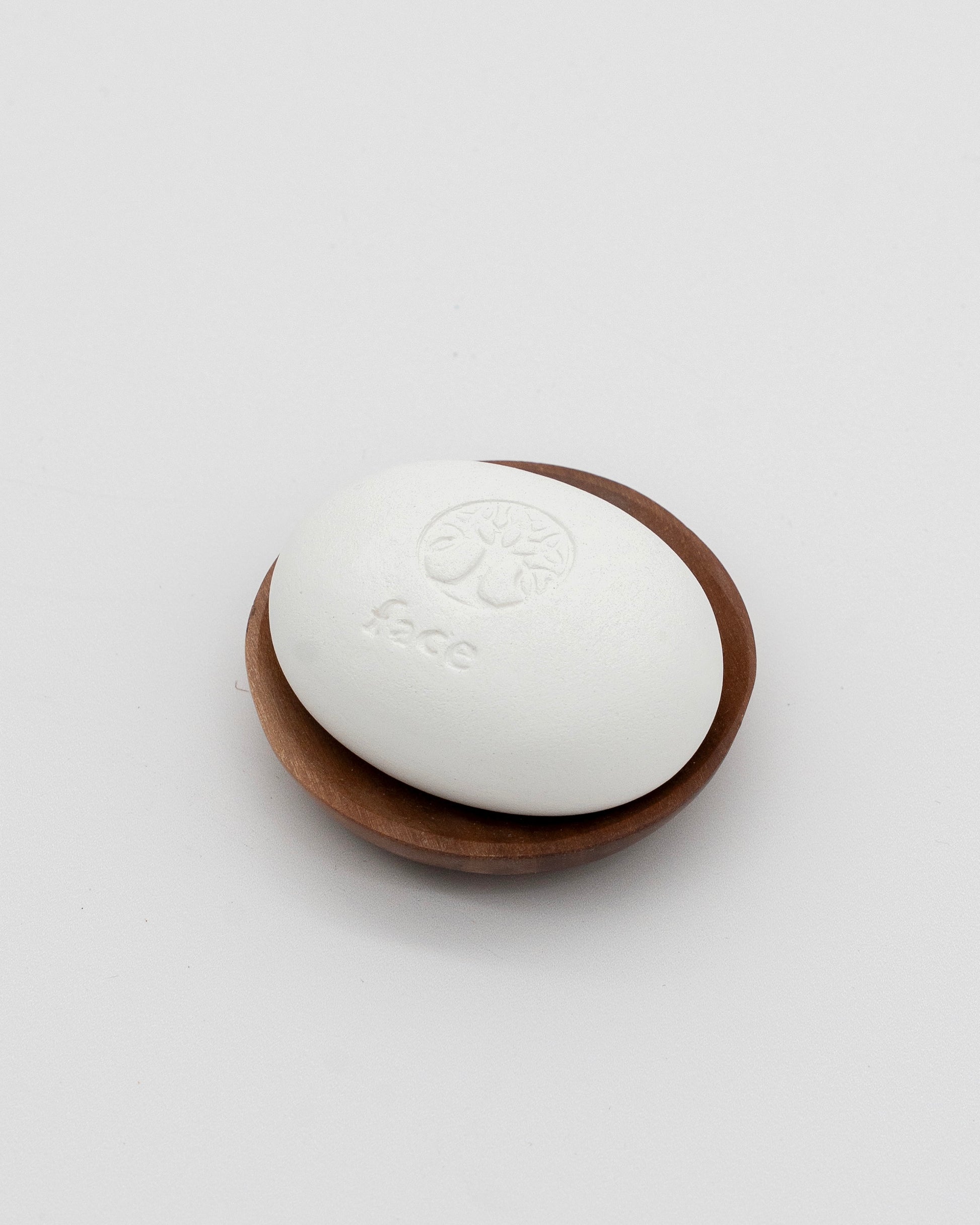 White smooth Face Pebble resting on a small wooden dish, designed for gentle exfoliation and myofascial massage.