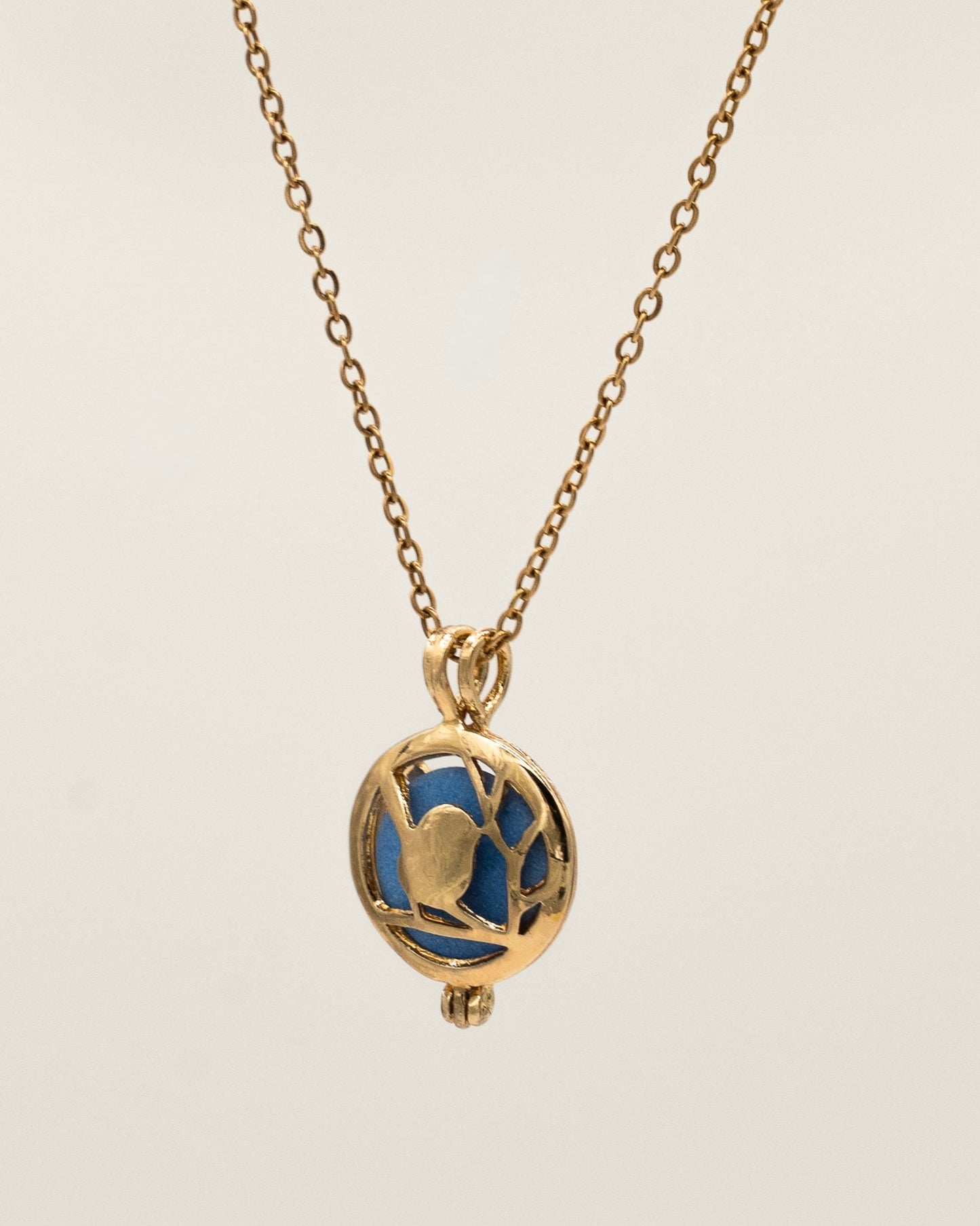 Gold Scent Locket featuring an intricate gold pendant with a blue interior stone on a delicate gold chain, designed as an aromatherapy necklace for a subtle fragrant experience.