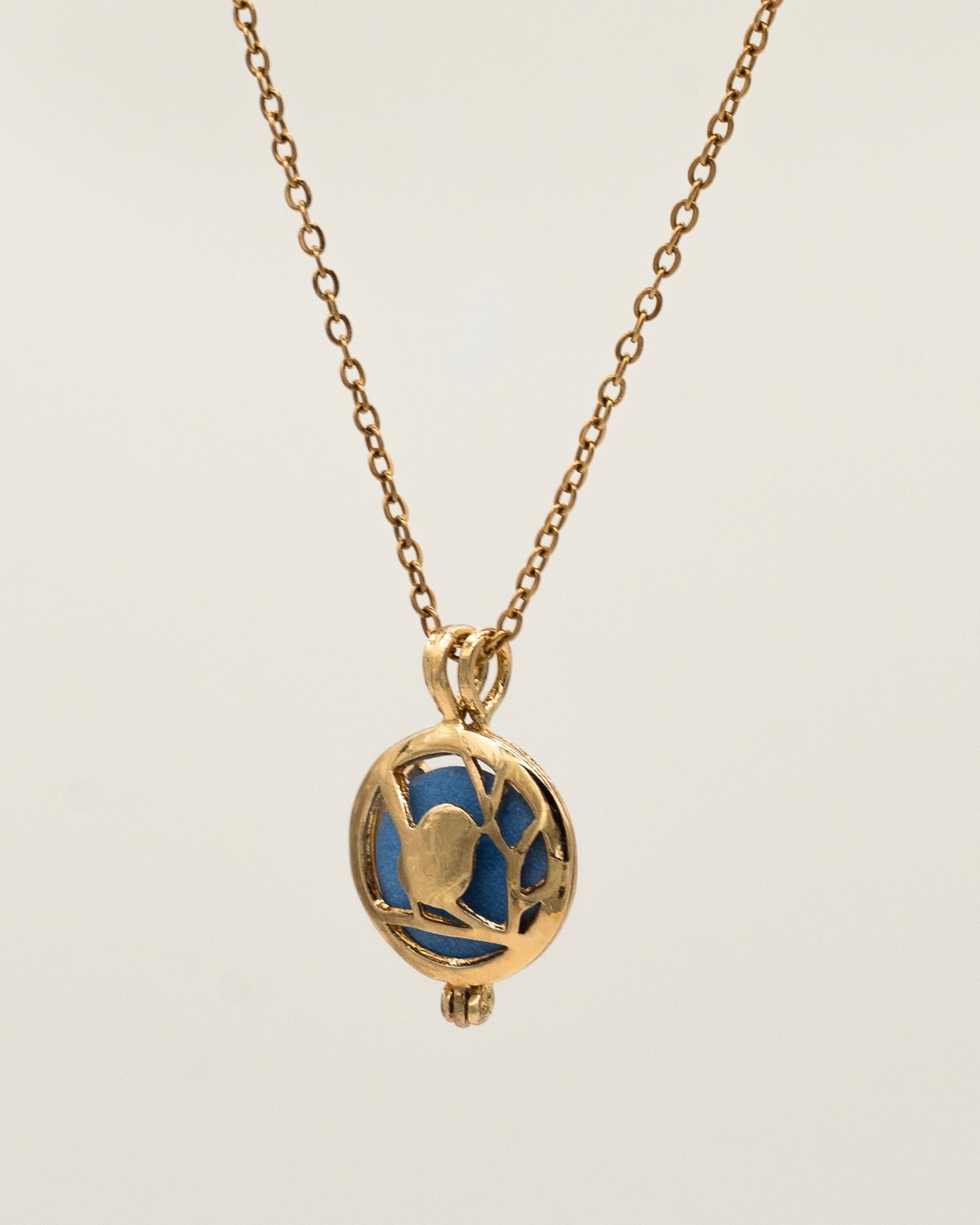 Gold Scent Locket featuring an intricate gold pendant with a blue interior stone on a delicate gold chain, designed as an aromatherapy necklace for a subtle fragrant experience.