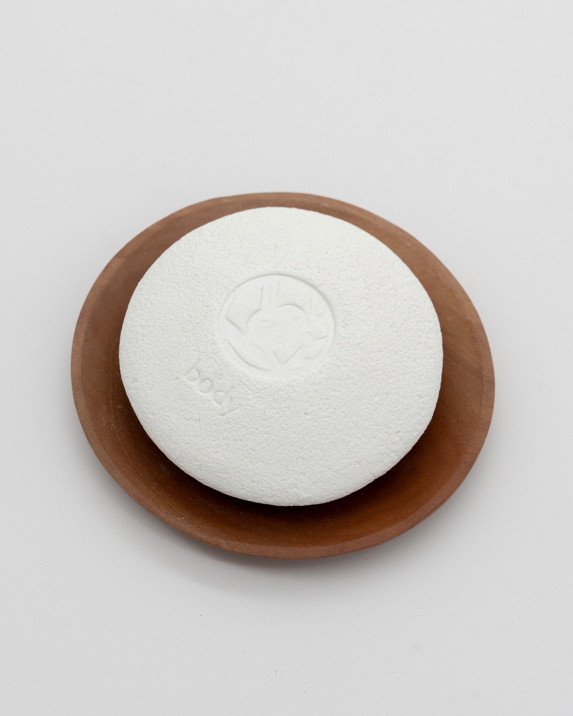 White textured Body Pebble resting on a smooth brown dish, designed for myofascial massage and exfoliate purposes.