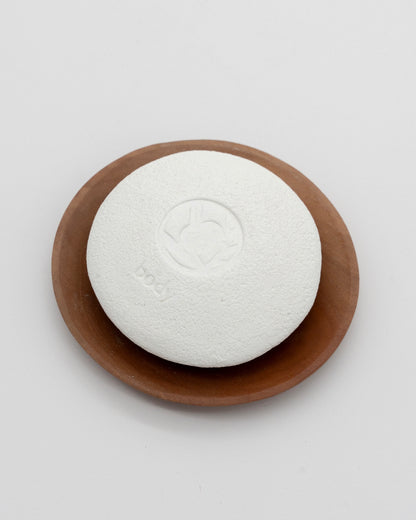White textured Body Pebble resting on a smooth brown dish, designed for myofascial massage and exfoliate purposes.