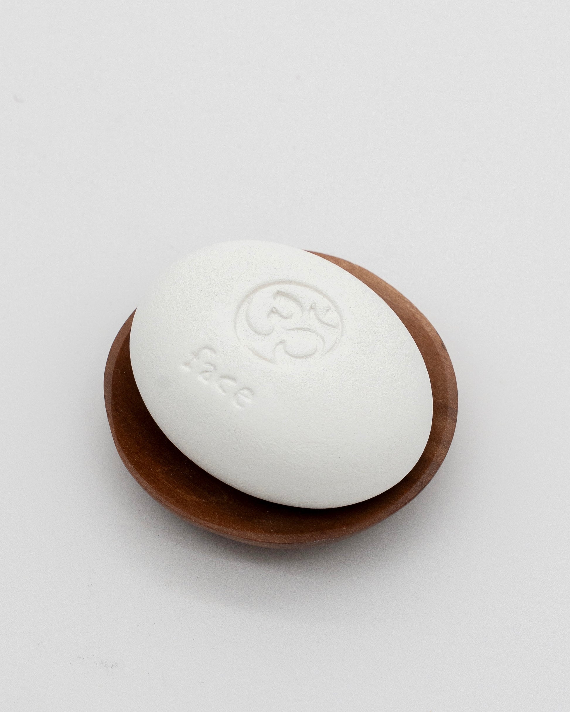 Face Pebble pumice stone placed on a small wooden dish, designed for gentle exfoliation and myofascial massage in skincare routines.