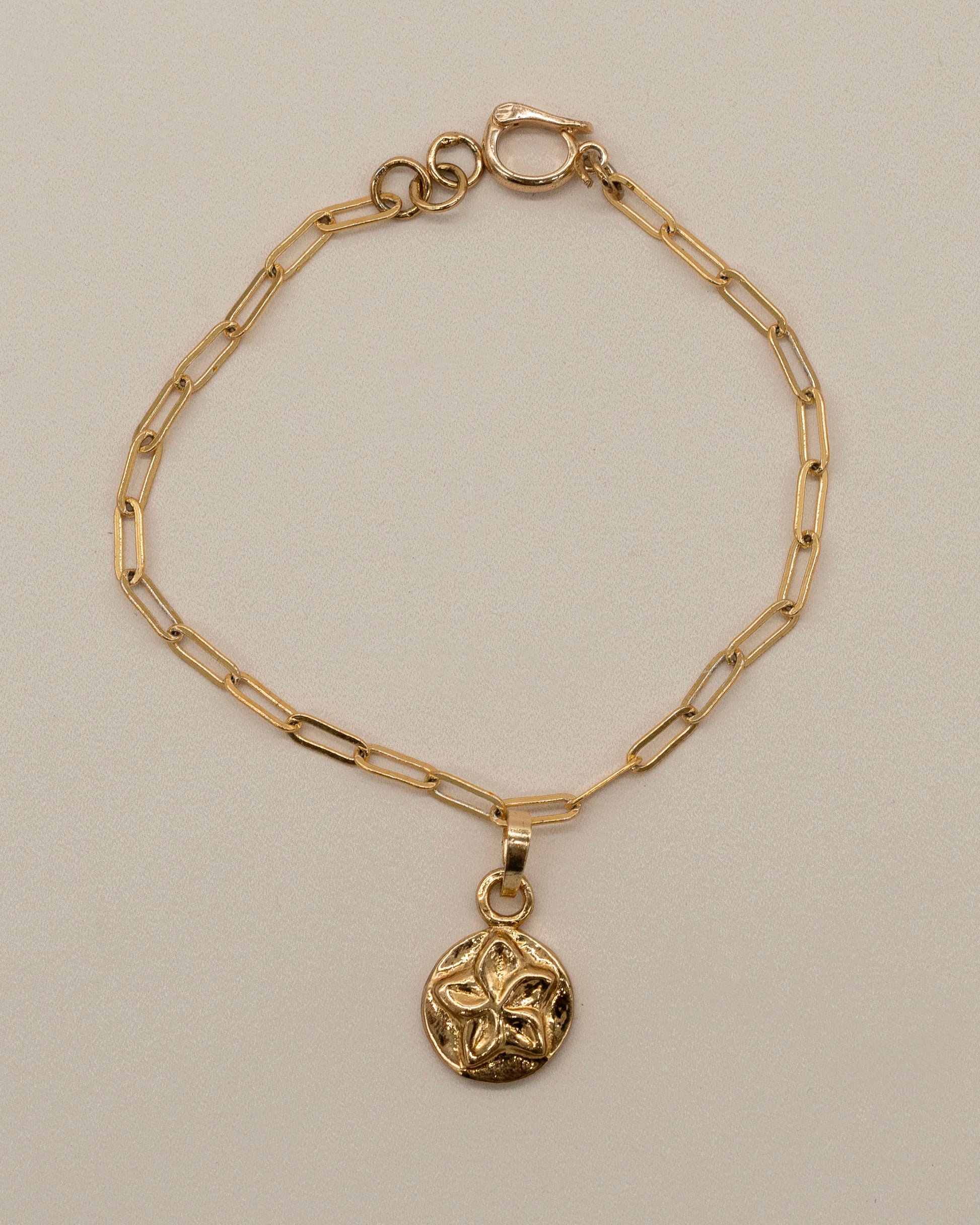 Charm Bracelet featuring a delicate gold chain with elongated links and a small polished circular pendant embossed with a floral design, minimalist and elegant.