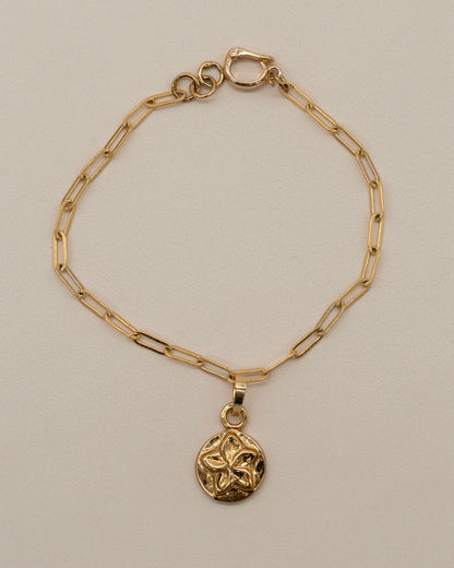 Charm Bracelet featuring a delicate gold chain with elongated links and a small polished circular pendant embossed with a floral design, minimalist and elegant.