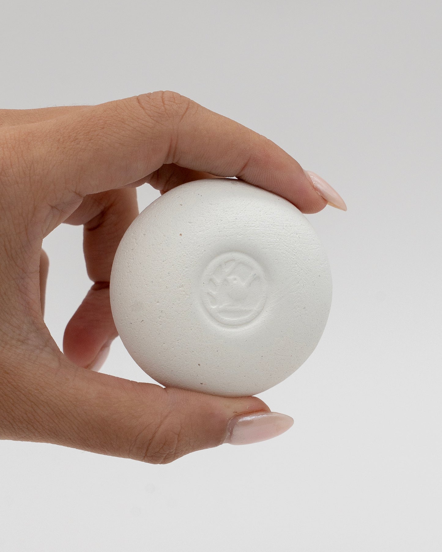 Hand holding a smooth white Scent Pebble with a subtle embossed design, highlighting its minimalist and eco-friendly aromatherapy accessory features.