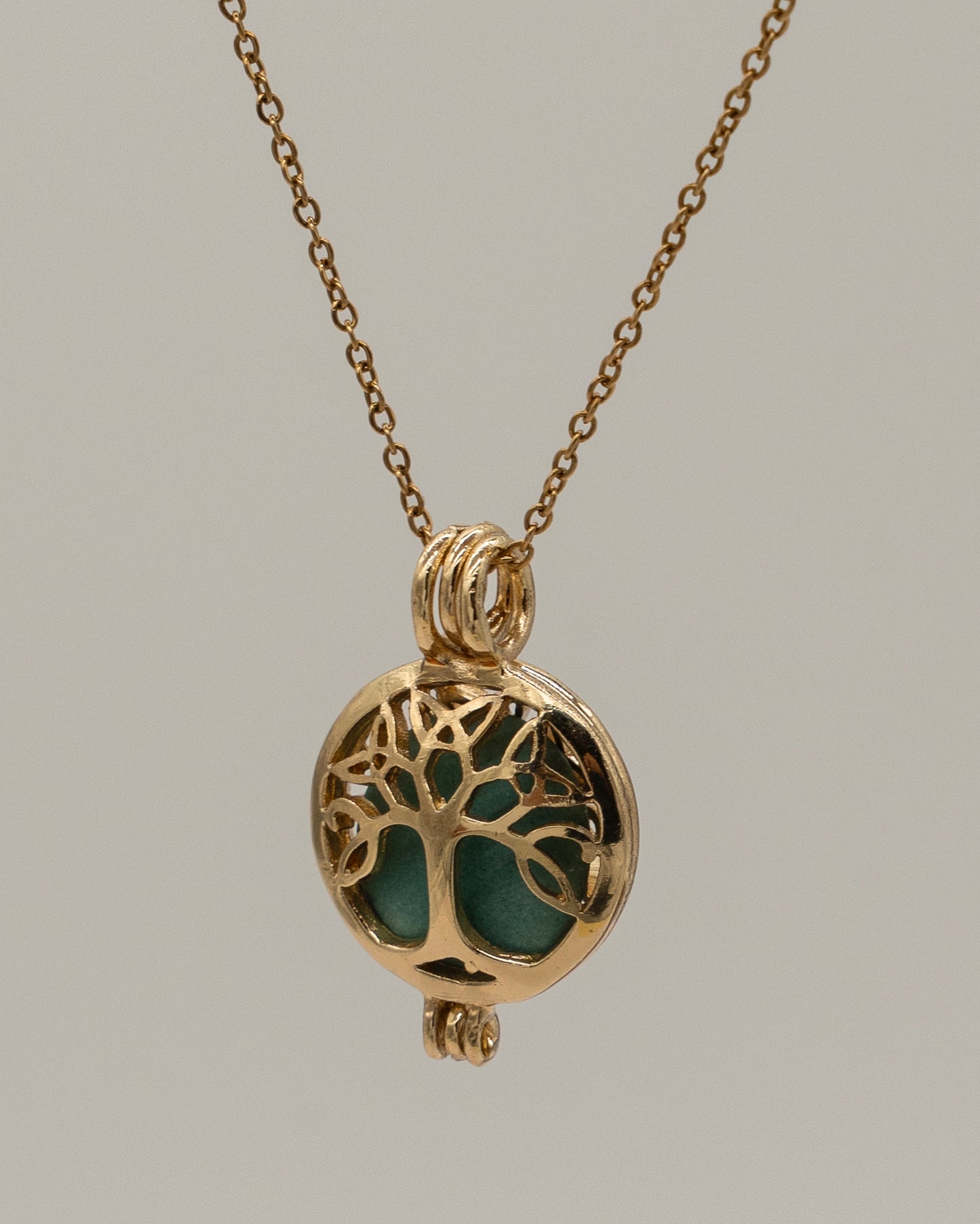 Gold Scent Locket necklace with an intricate tree design and a green aromatic stone inside, offering a stylish aromatherapy accessory.