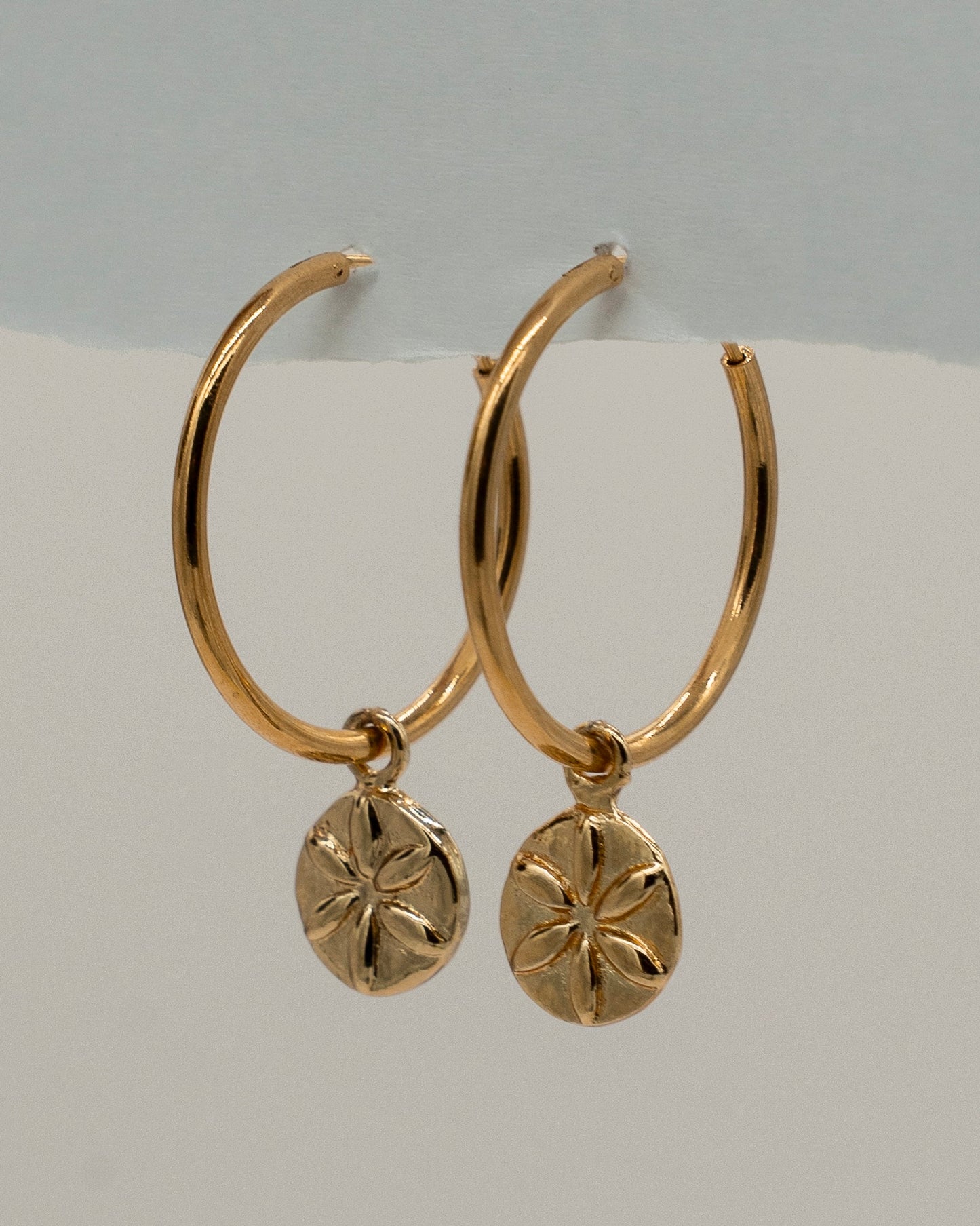Pair of elegant gold hoop Charm Earrings featuring small round pendants with a flower-like engraved design, perfect for everyday or special occasions.