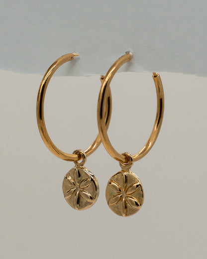 Pair of elegant gold hoop Charm Earrings featuring small round pendants with a flower-like engraved design, perfect for everyday or special occasions.