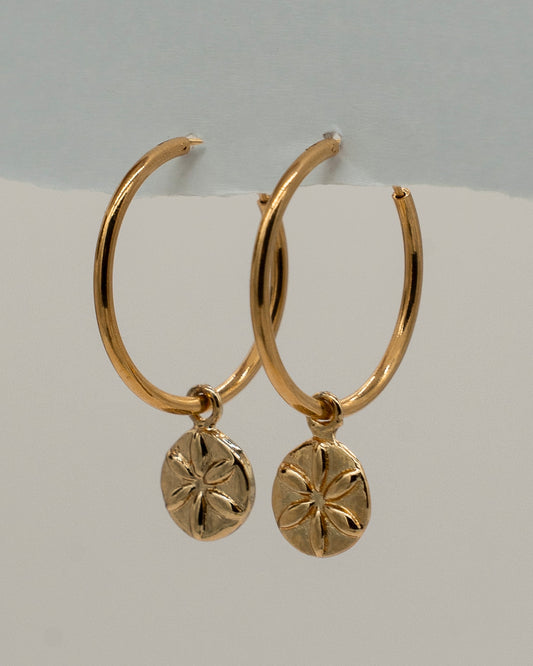 Pair of elegant gold hoop Charm Earrings featuring small round pendants with a flower-like engraved design, perfect for everyday or special occasions.
