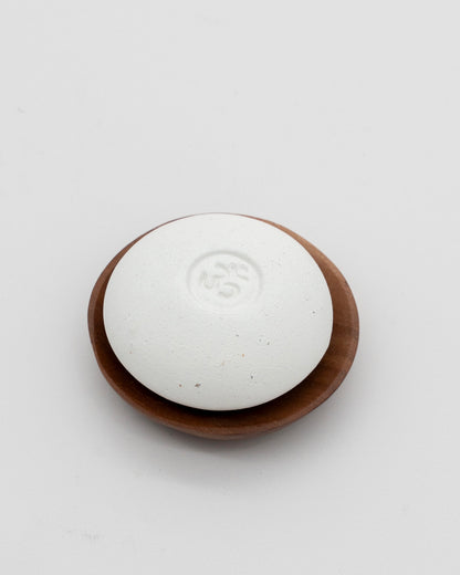 Scent Pebble, a smooth white aromatherapy stone with embossed detail, resting on a round wooden dish, designed for eco friendly relaxation and fragrance diffusion.