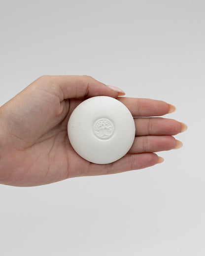 Hand holding a smooth white Scent Pebble with an embossed tree design, showcasing its compact, eco-friendly aromatherapy stone ideal for relaxation and myofascial massage.