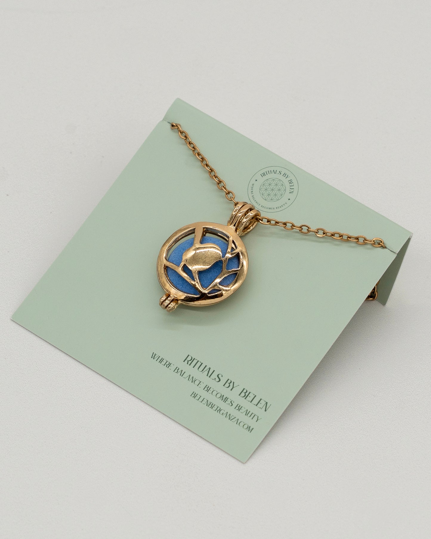 Gold Scent Locket with a delicate gold chain and intricate floral design, featuring a blue aromatherapy diffuser center on a minimalist display card.