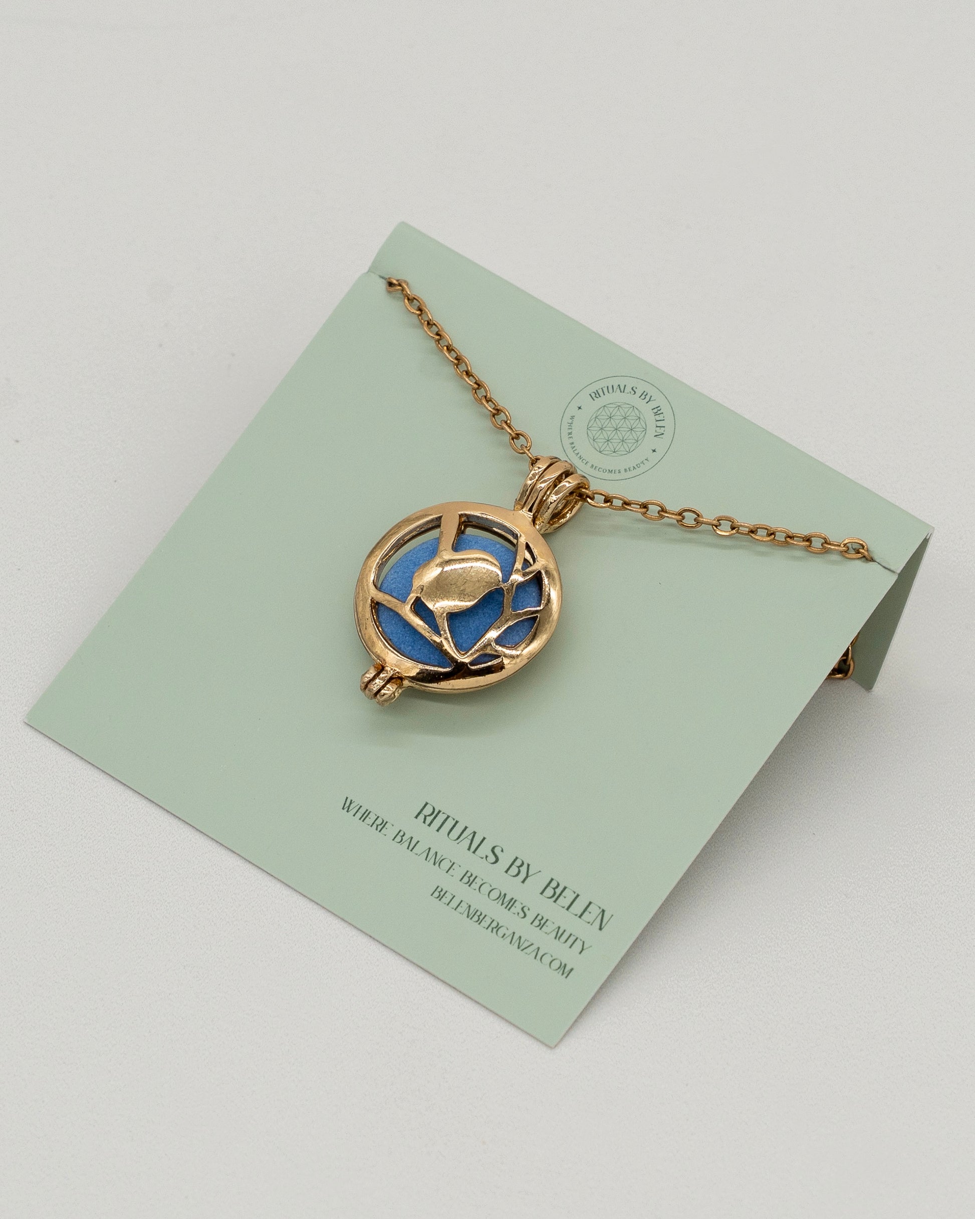 Gold Scent Locket with a delicate gold chain and intricate floral design, featuring a blue aromatherapy diffuser center on a minimalist display card.