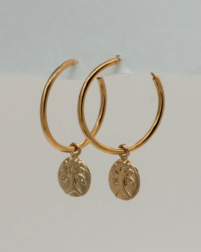 Gold hoop earrings with circular pendants on a light gray background