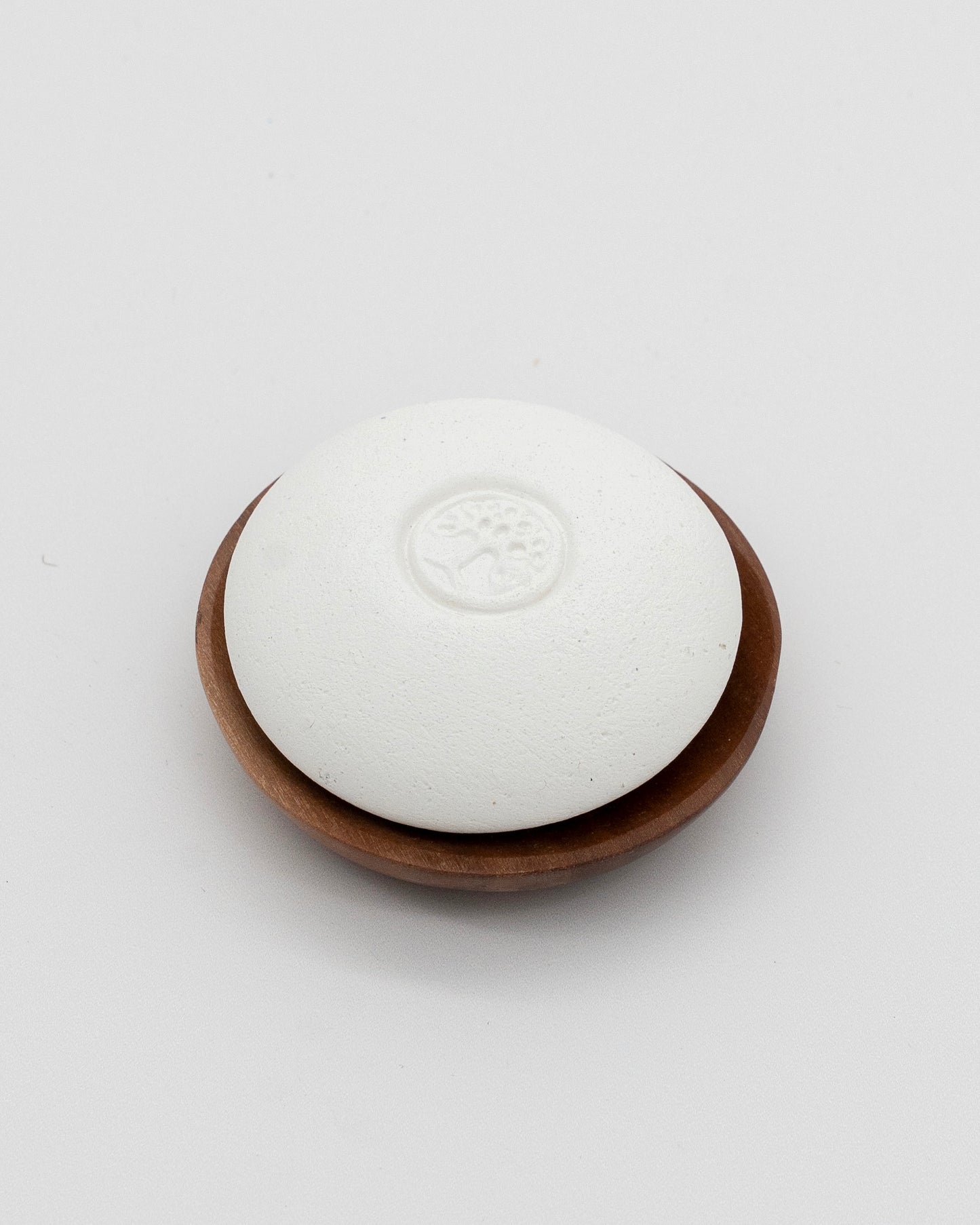 White Scent Pebble pumice stone with a tree emblem, resting on a small wooden dish, designed for exfoliation and aromatherapy purposes.