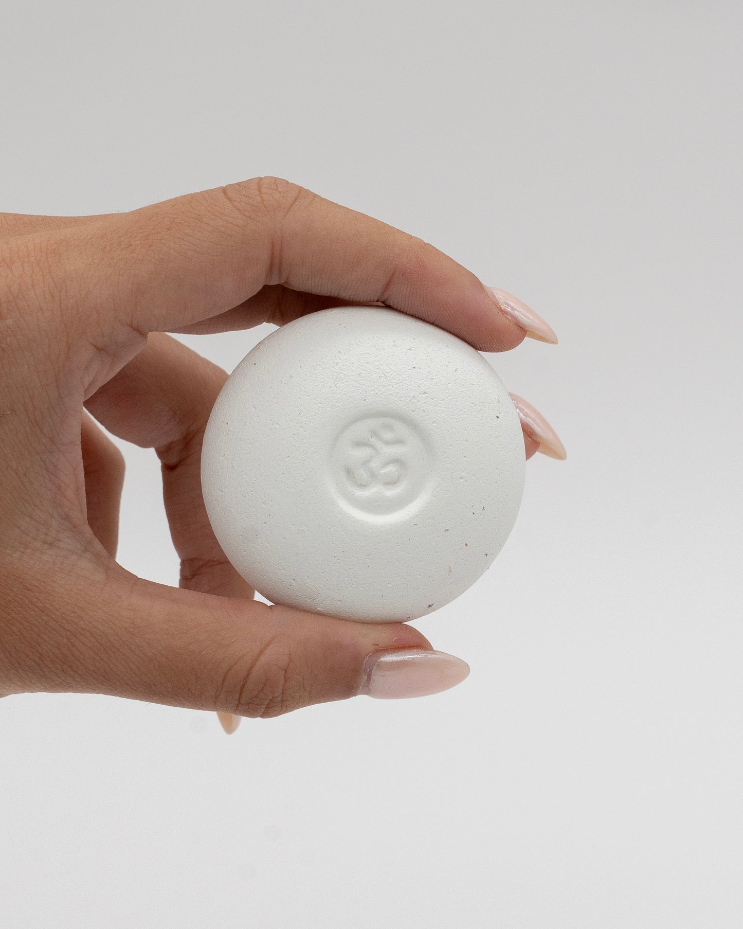 Hand holding a smooth white Scent Pebble with a subtle embossed symbol in the center against a neutral background, highlighting its minimalist design.