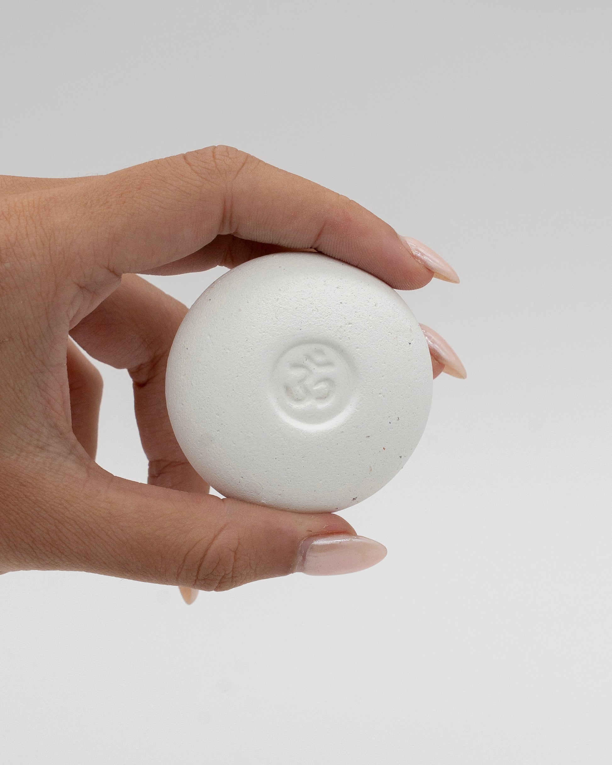 Hand holding a smooth white Scent Pebble with a subtle embossed symbol in the center against a neutral background, highlighting its minimalist design.