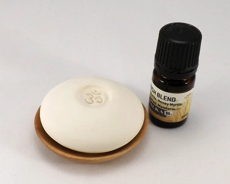 Scent Pebble resting on a small wooden dish next to a bottle of essential oil blend, designed for aromatherapy and creating a calming atmosphere.