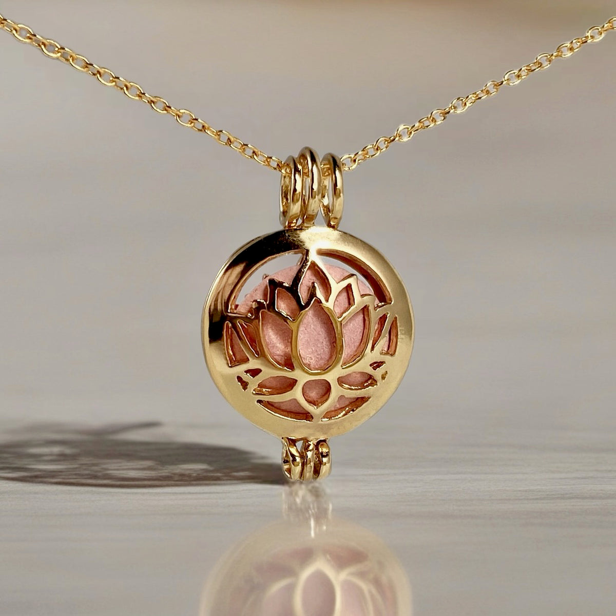 gold locket in a chain with a lotus design and a pink stone inside