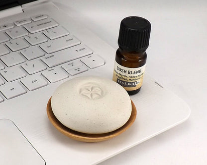 Scent Pebble aromatherapy diffuser placed on a small wooden dish next to a bottle of essential oil on a laptop keyboard, promoting relaxation and eco friendly wellness.