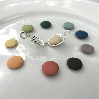 colour options of pebbles in a white dish with an open silver locket in the middle