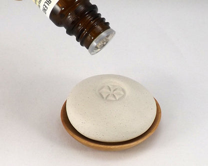 Scent Pebble placed on a small wooden dish with an essential oil bottle positioned above, illustrating use in aromatherapy and scent diffusion.