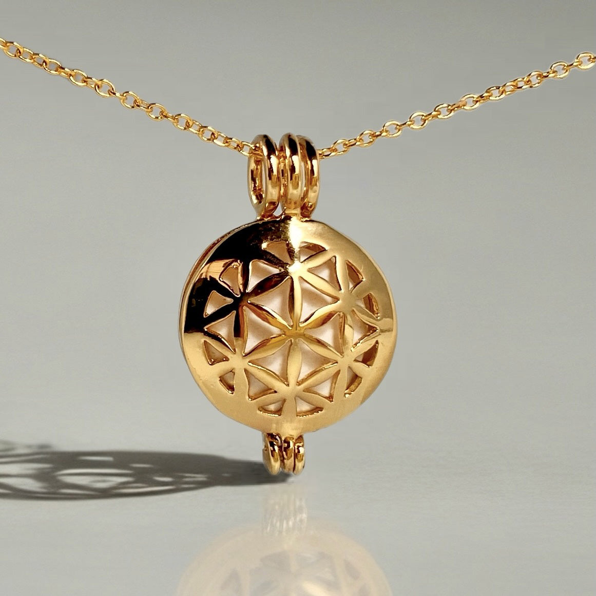 gold locket in a chain with a flower of life pattern design and a orange stone inside