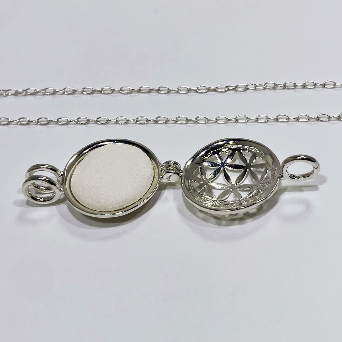 silver locket open with a white stone inside and a chain in a white background