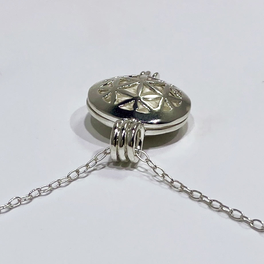 silver locket top view with a white stone inside and a chain in a. white background